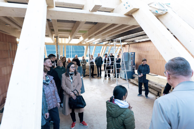 Das Bild zeigt ca. 20 Personen zum Richtfest in einem ungedeckten, offenen Dachstuhl.