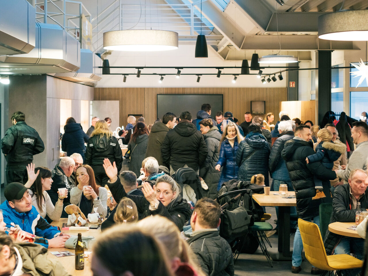 Das Bild zeigt viele Personen in einer größeren Halle stehend und sitzend.