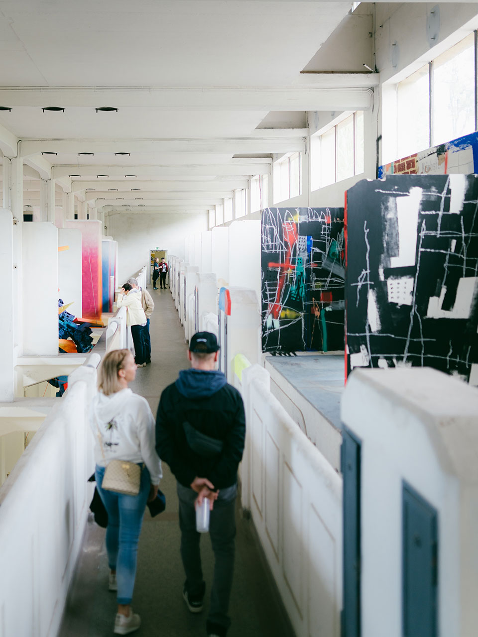 Das Bild zeigt einen langen Gang im Umspanwerk Etzdorf. Die Wände sind alle weiß gestrichen. Links und rechts sind ein paar künstlerisch bemalte Flächen zu sehen. Im Gang stehen ein paar Menschen.